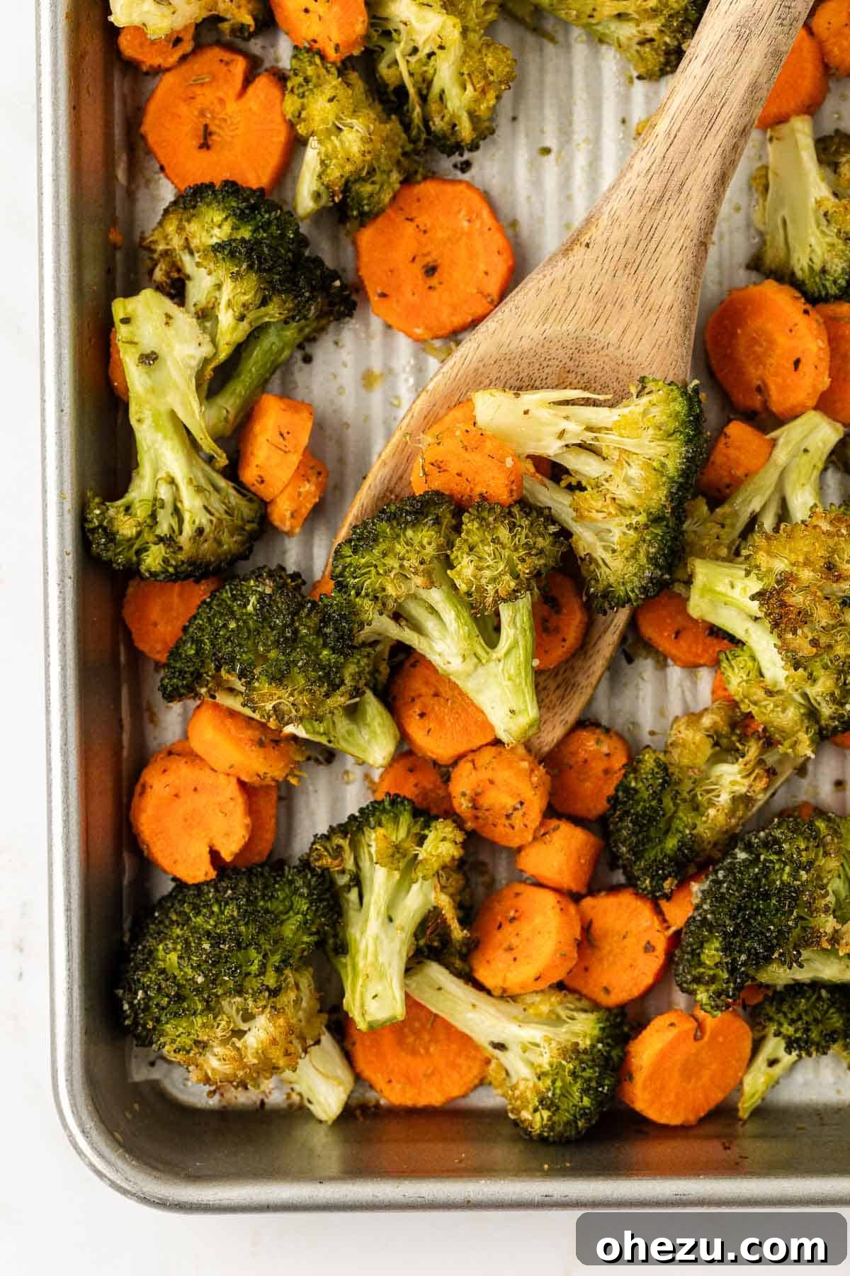 A close-up shot of perfectly roasted broccoli and carrots on a baking sheet, with a wooden serving spoon nearby, ready to be enjoyed.