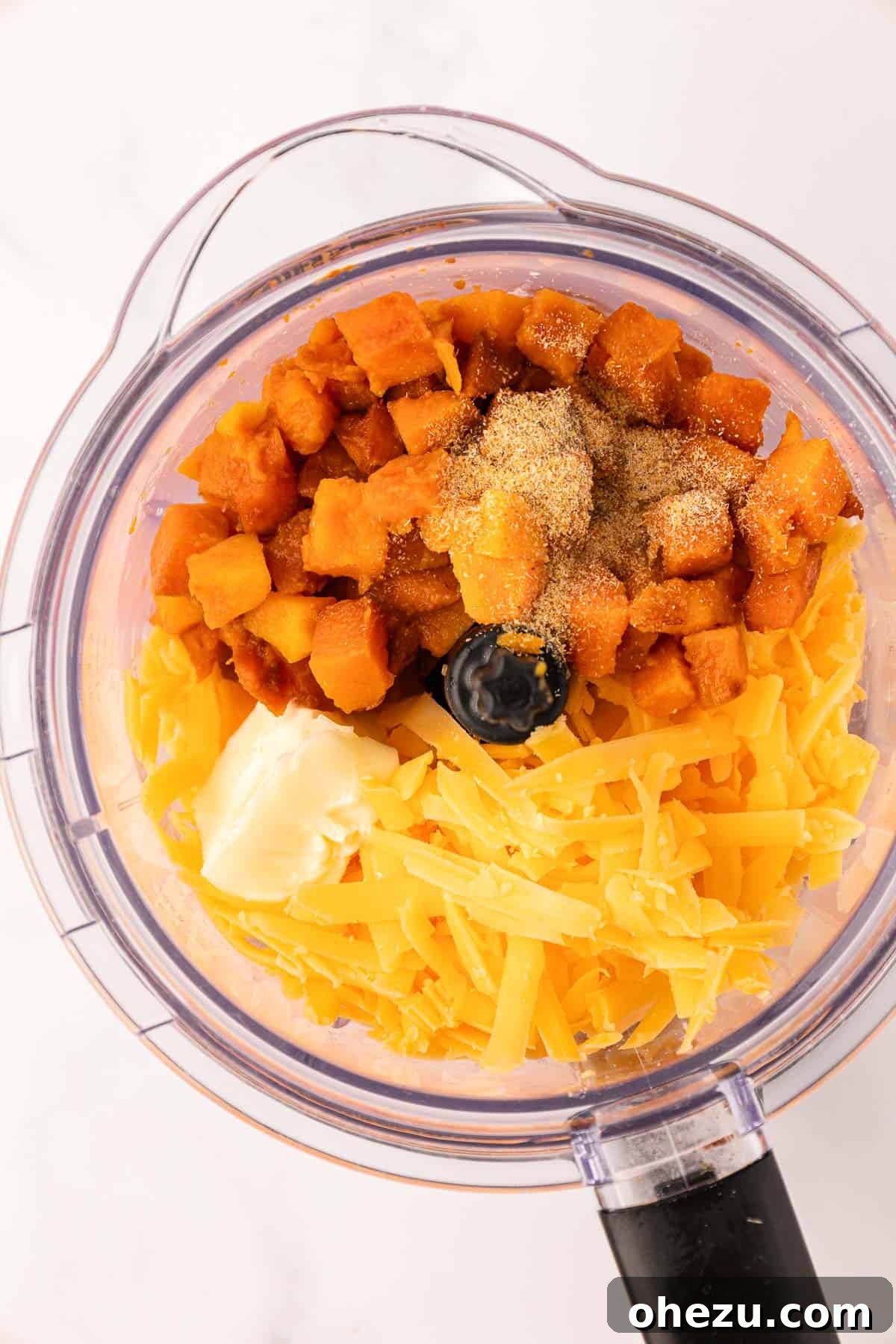 Butternut squash, spices, cheese, and butter placed in a food processor, ready for blending.