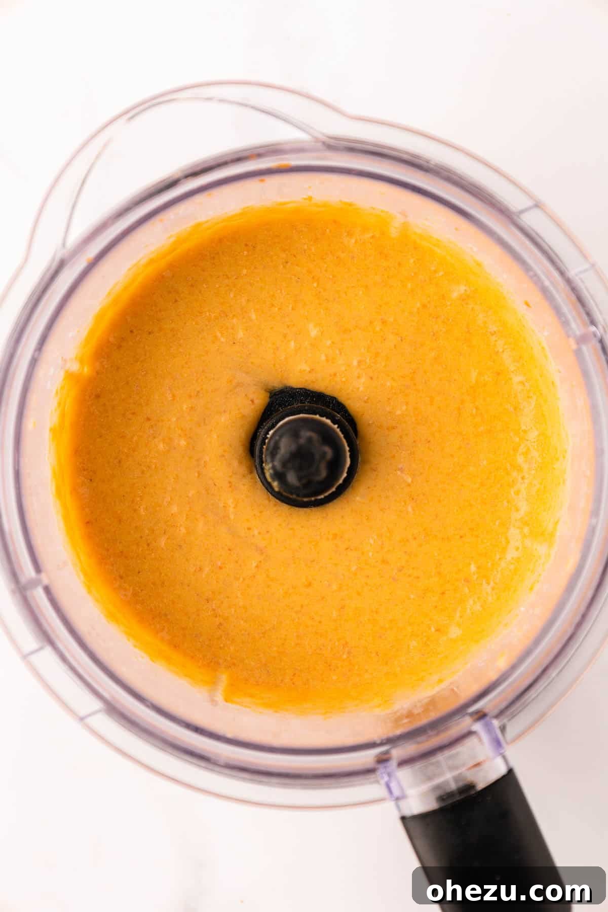 A close-up shot of the smooth, vibrant orange cheese sauce swirling in the food processor after blending.