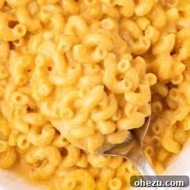 A close-up of the butternut squash mac and cheese with a serving spoon, illustrating the recipe.