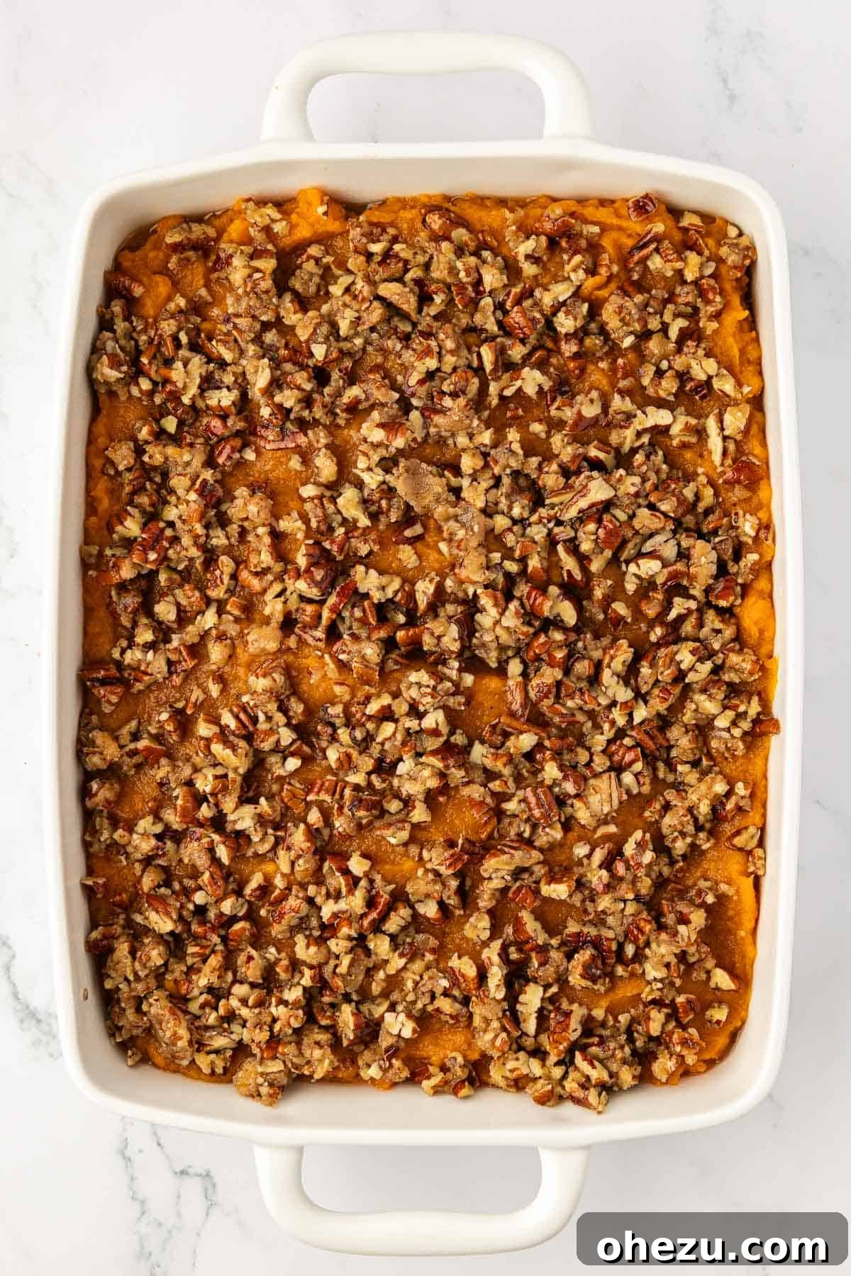 A sweet potato casserole topped with a thick layer of pecan crumble, ready to be baked to golden perfection.