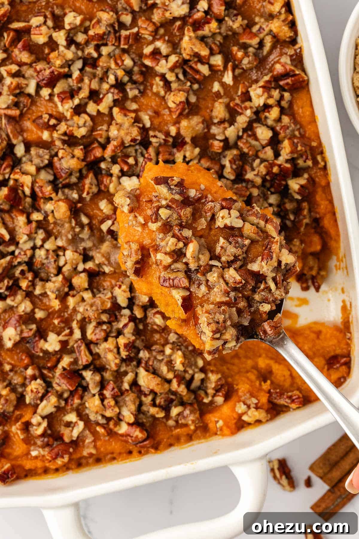 A serving spoon filled with sweet potato casserole and pecan topping, glistening and ready to be served.