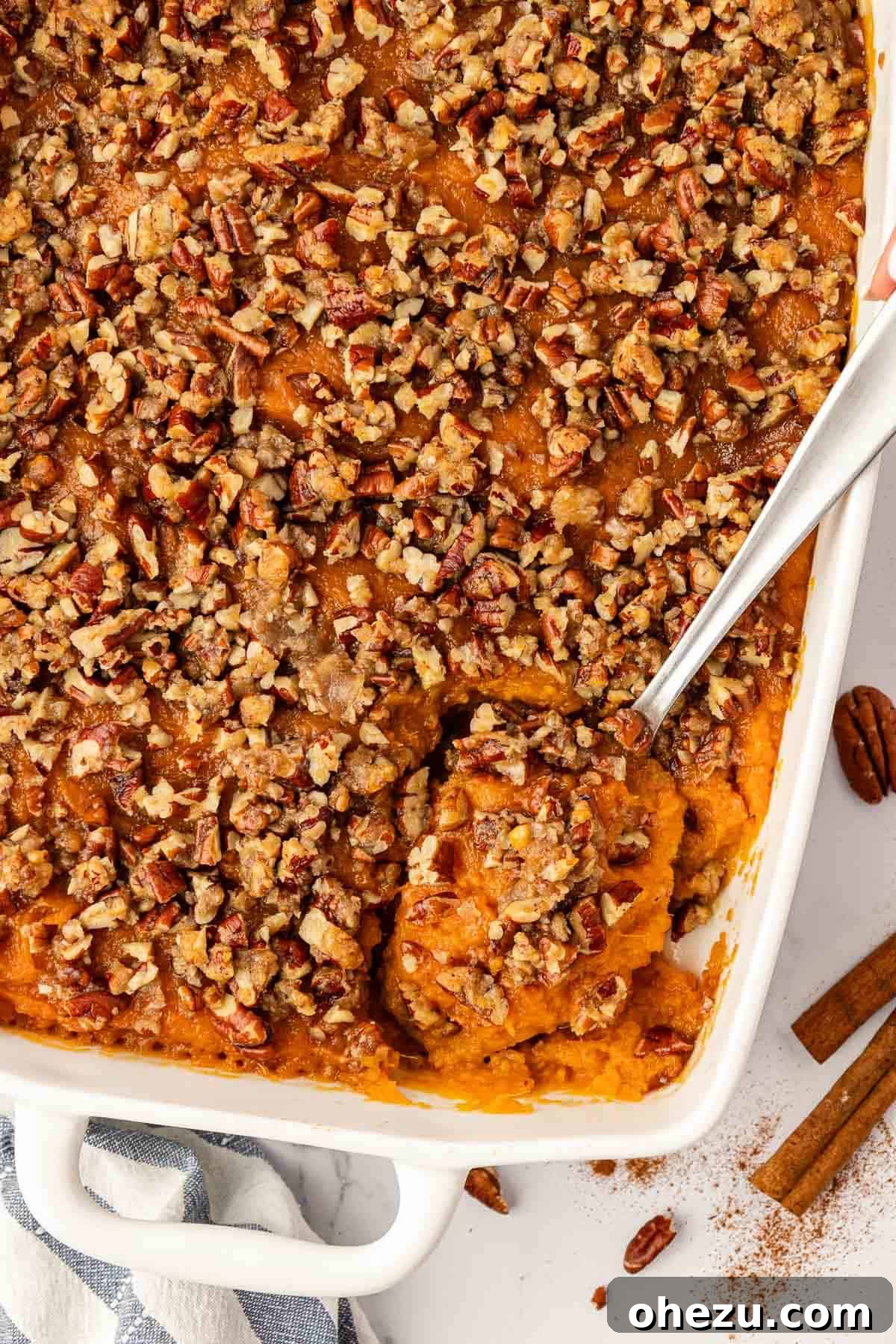 A festive sweet potato casserole with pecans in a baking dish, surrounded by holiday decor, inviting guests to enjoy.