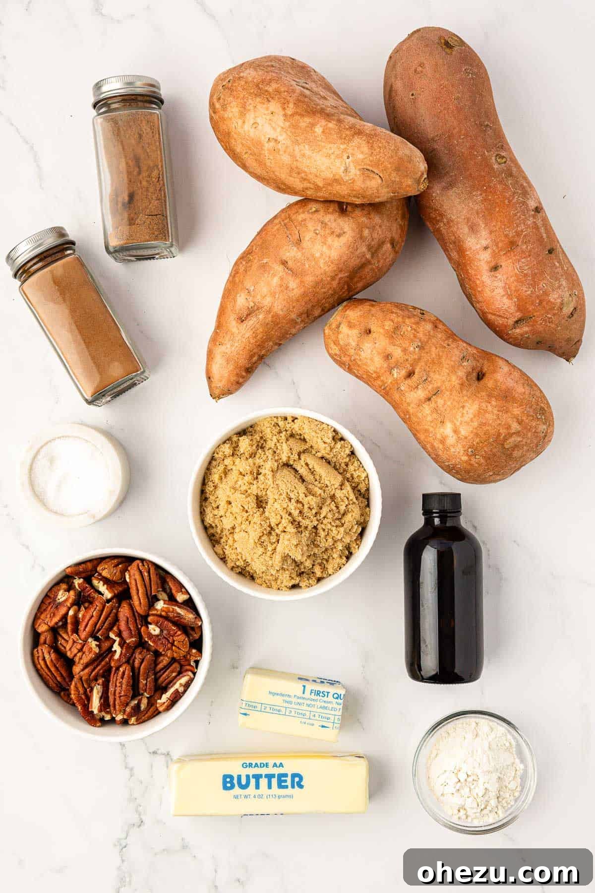 A flat lay photograph showcasing all the fresh ingredients required to make a sweet potato casserole with pecans, including whole sweet potatoes, butter, brown sugar, spices, flour, and chopped pecans.