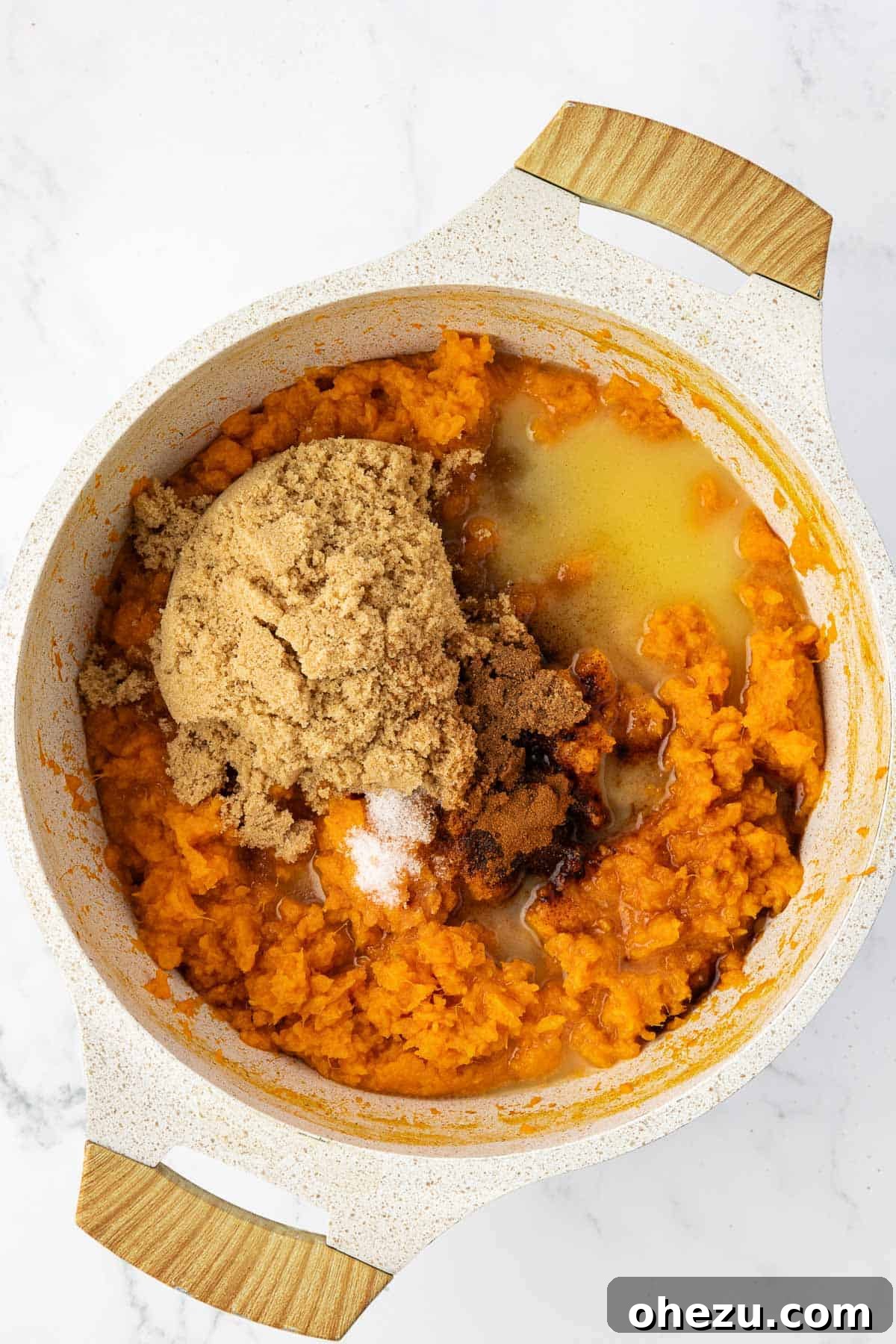 Adding melted butter, brown sugar, and spices to the mashed sweet potatoes in a saucepan, preparing the rich filling.