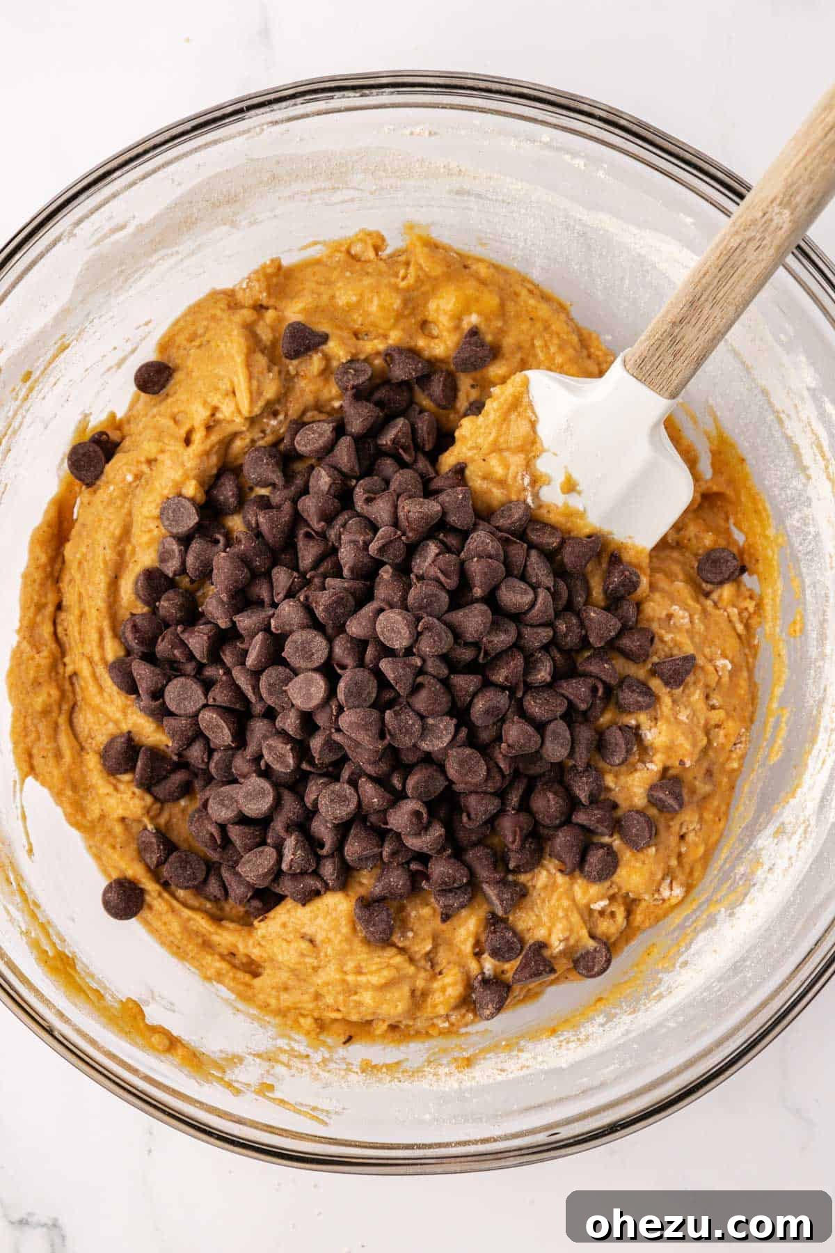 Semi-sweet chocolate chips being added to the pumpkin muffin batter in a mixing bowl, ready for folding.