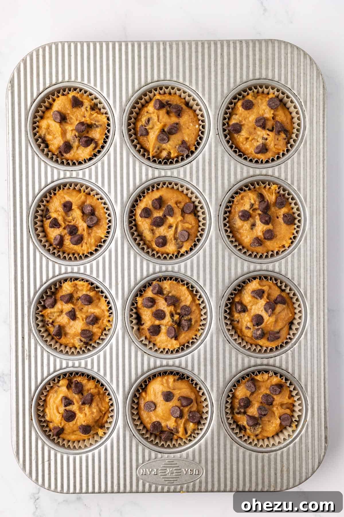 Pumpkin chocolate chip muffin batter portioned evenly into a muffin tin lined with parchment paper cups, ready for baking.