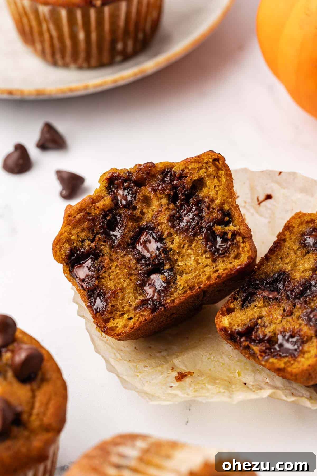 A pumpkin chocolate chip muffin cut in half, revealing its moist, tender interior studded with melted chocolate chips, demonstrating its perfect texture.
