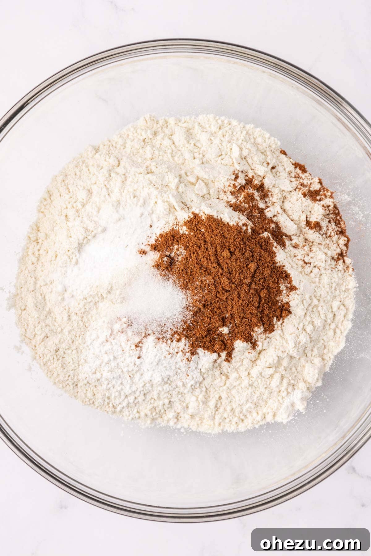 A mixing bowl filled with dry ingredients: flour, salt, baking powder, baking soda, and pumpkin pie spice, ready to be whisked together.