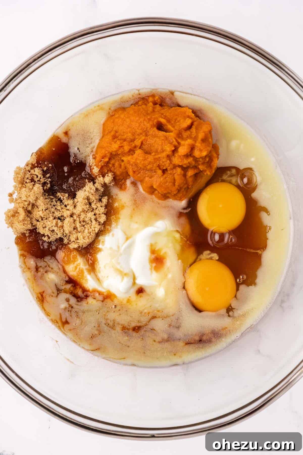 A bowl filled with all the wet ingredients for pumpkin muffins: Greek yogurt, pumpkin puree, melted butter, eggs, vanilla extract, maple syrup, and brown sugar, before mixing.