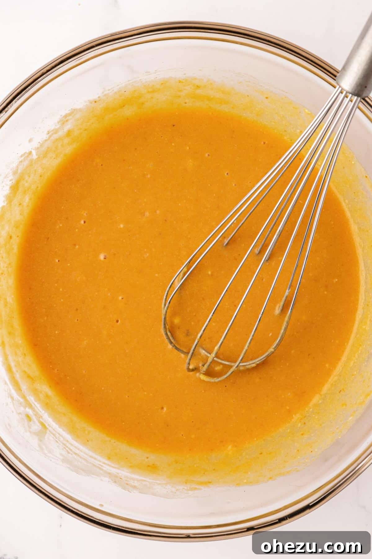 A whisk vigorously mixing the wet ingredients together in a bowl, creating a smooth, orange-hued mixture for the pumpkin muffins.