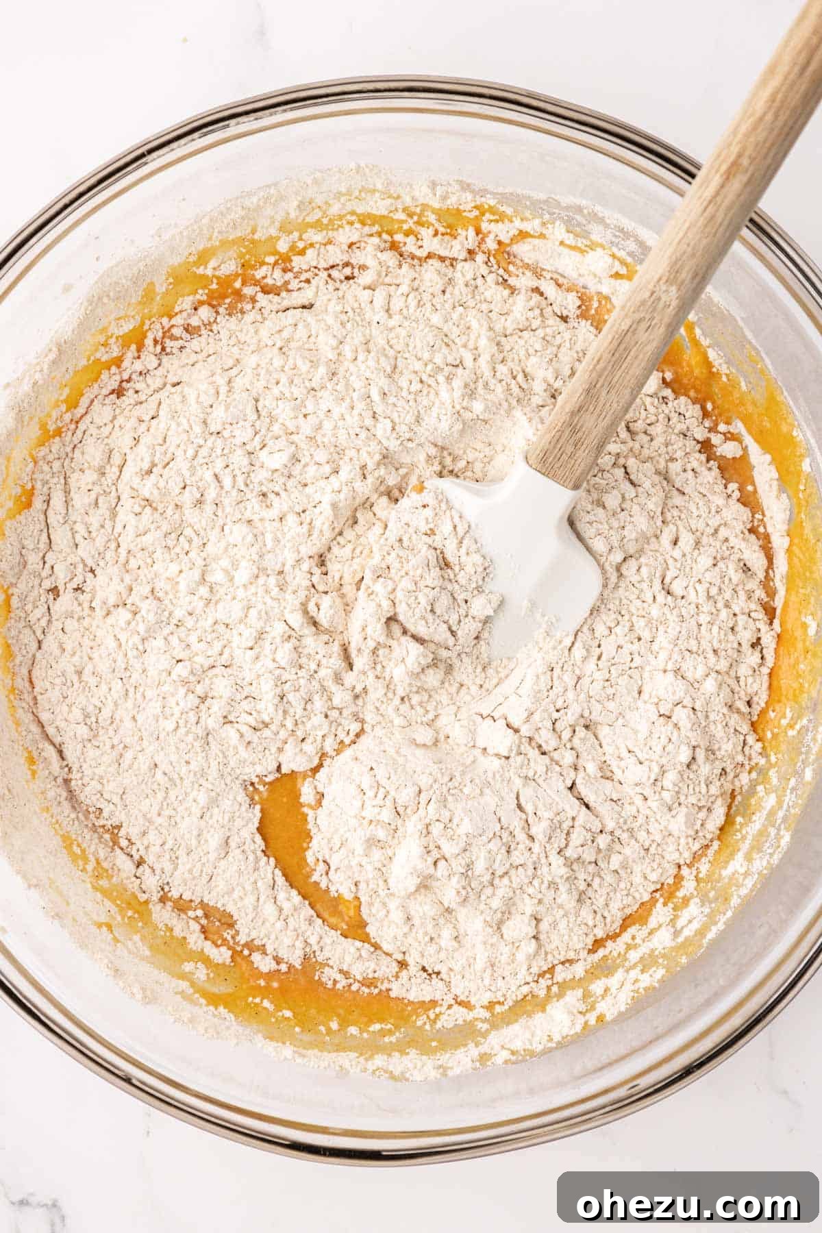 The process of adding the dry flour mixture to the wet pumpkin mixture in a bowl, ready to be gently folded together.