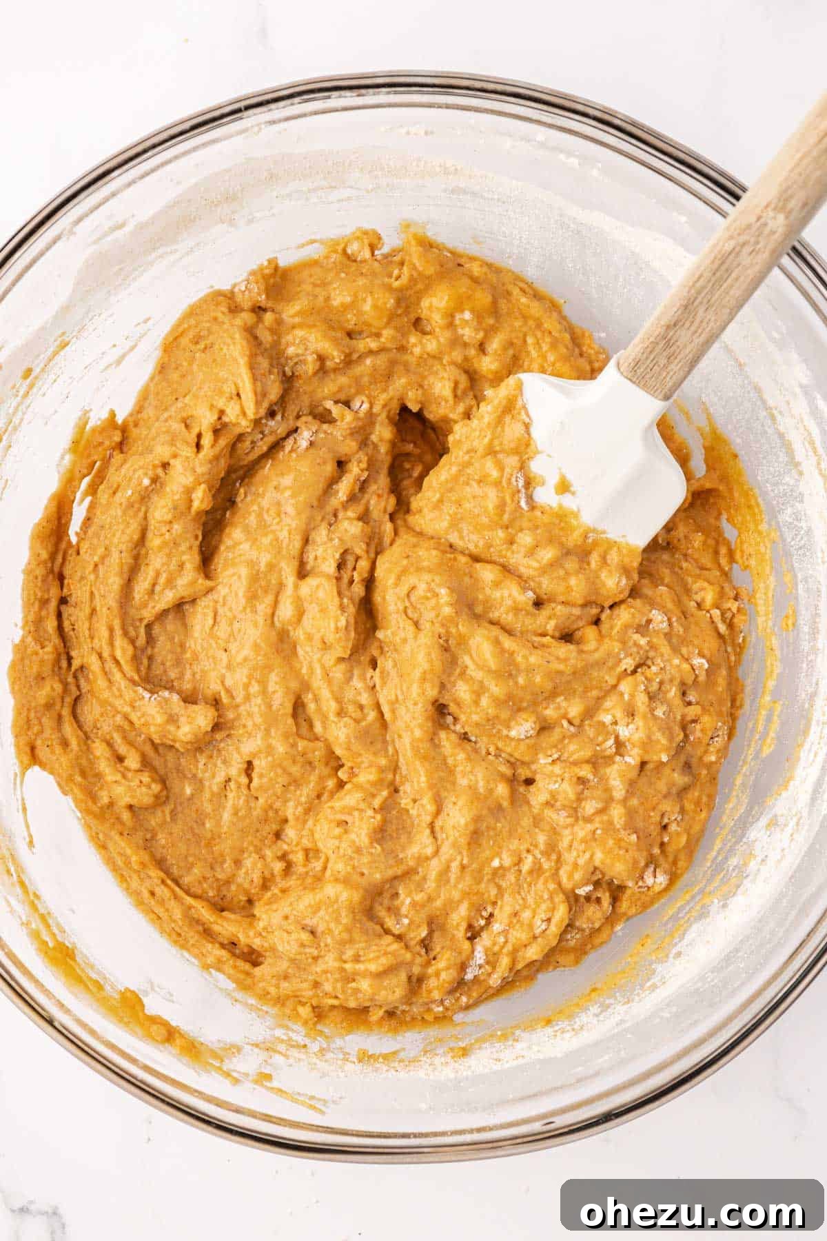 A close-up of the pumpkin muffin batter after the wet and dry ingredients have been gently combined, showing a thick, uniform consistency with no dry streaks.