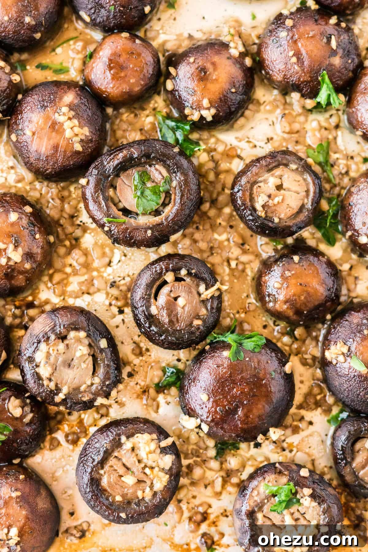 Close-up of golden brown roasted garlic mushrooms on a baking sheet, glistening with garlic butter.