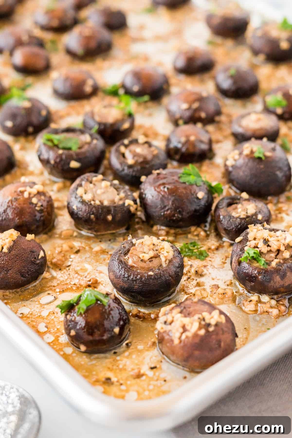 Two baking sheets side-by-side, one with fresh mushrooms and the other with garlic butter drizzled over them.