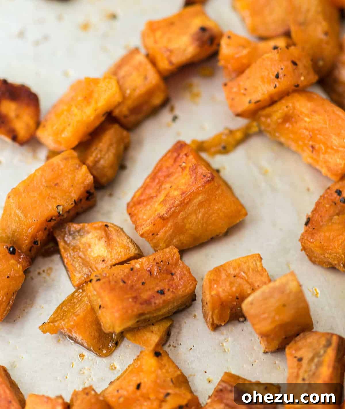 A close-up of seasoned sweet potato cubes on a baking sheet, ready for roasting.