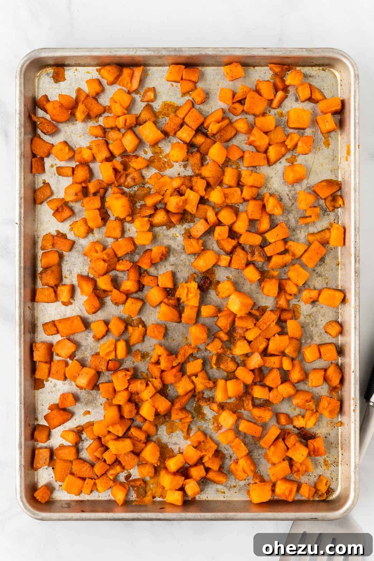 Crispy roasted sweet potato cubes with golden edges on a baking sheet, just out of the oven.