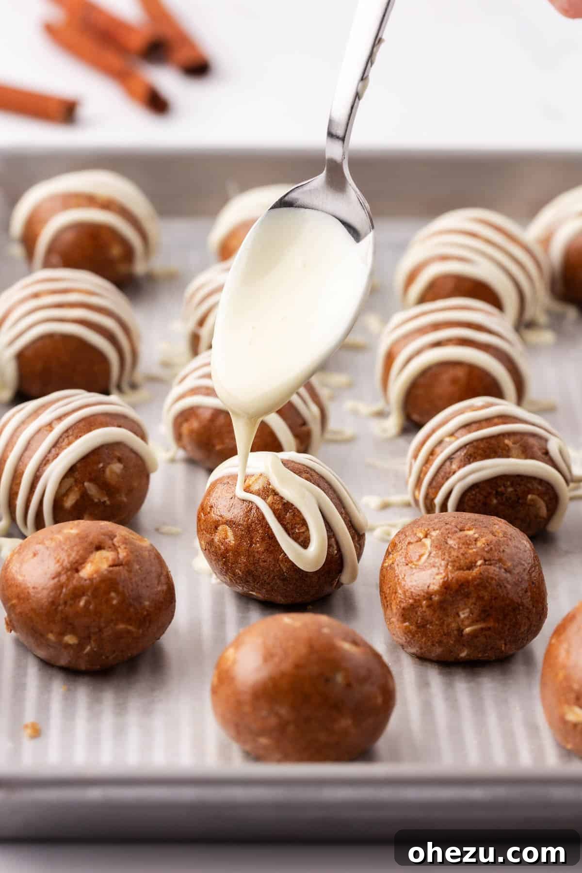 drizzling white chocolate over energy bites on a baking sheet