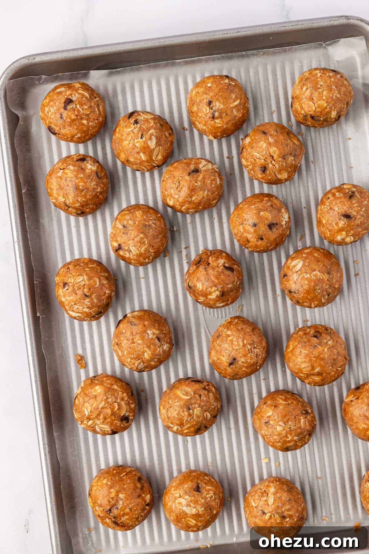 Finished oatmeal cookie energy balls chilling on a wax paper-lined baking sheet.