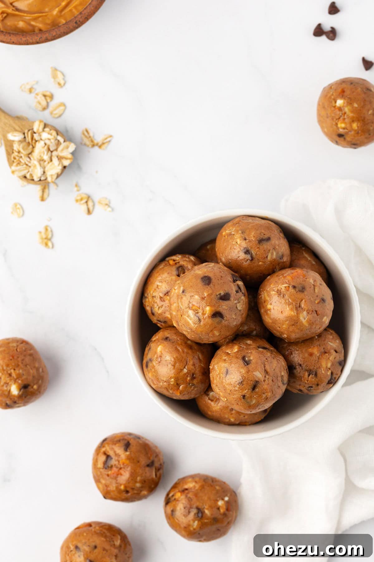A stack of three peanut butter pretzel energy bites on a rustic wooden board, garnished with pretzels and chocolate chips