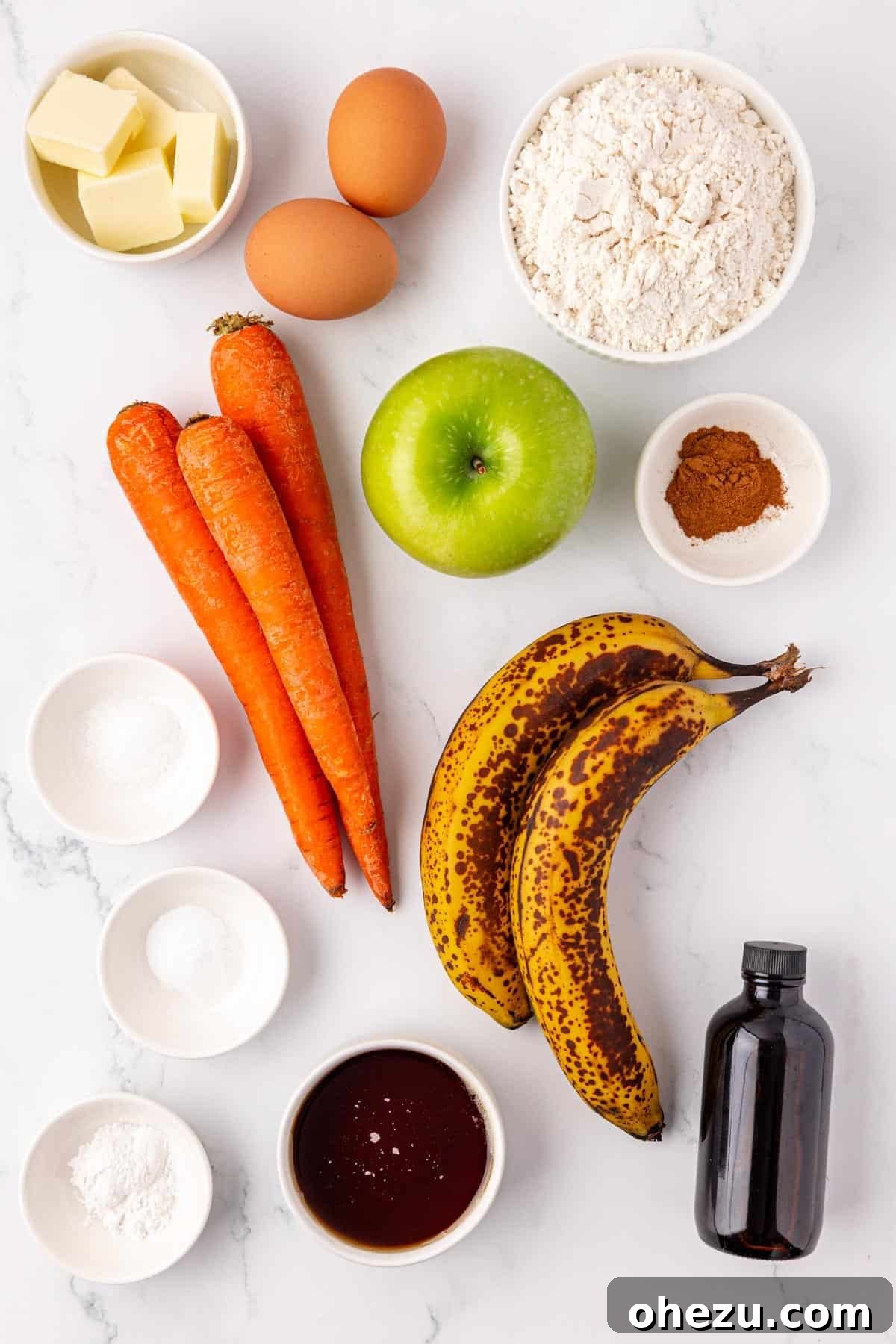Poppable Perfection Muffins 4 A flat lay photograph showcasing all the fresh ingredients laid out before baking ABC mini muffins, including bananas, apples, carrots, flour, and maple syrup.