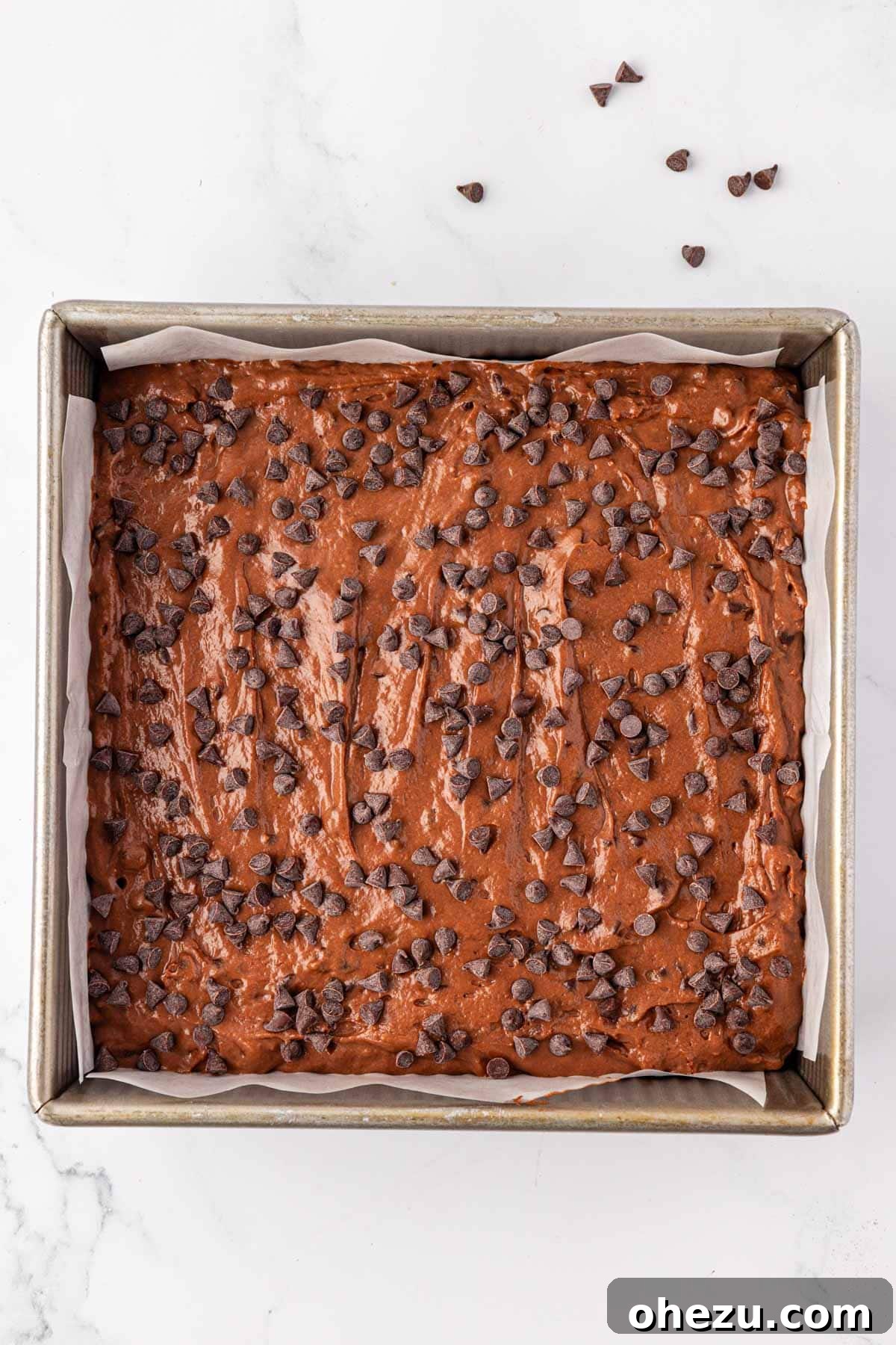 Chocolate snack cake batter in a parchment-lined pan topped with chocolate chips