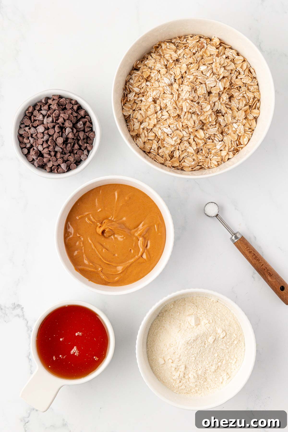 A collection of ingredients for protein granola bars, including natural creamy peanut butter, honey, vanilla protein powder, rolled oats, salt, and mini chocolate chips, neatly laid out on a kitchen counter.