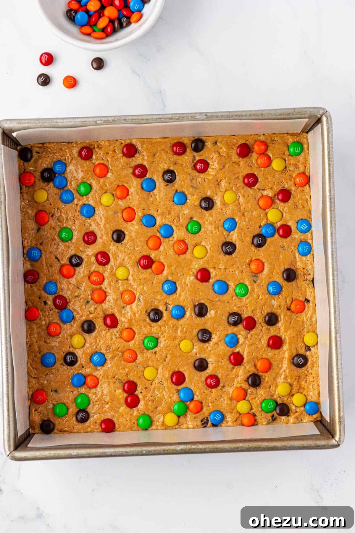Monster cookie protein bar batter with M&M's pressed into a pan, ready for chilling