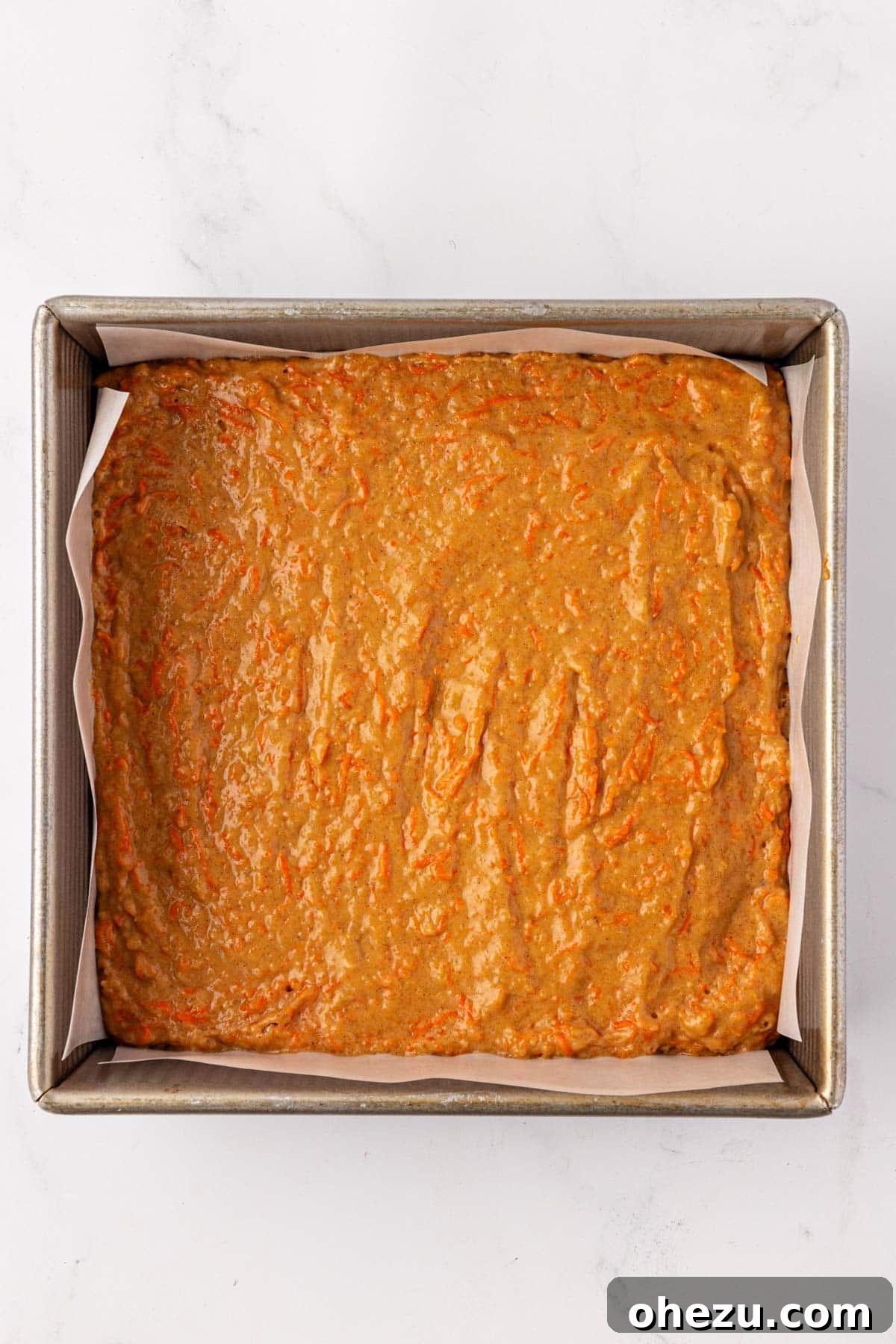 Carrot cake batter evenly spread in an 8x8 inch baking dish lined with parchment paper.