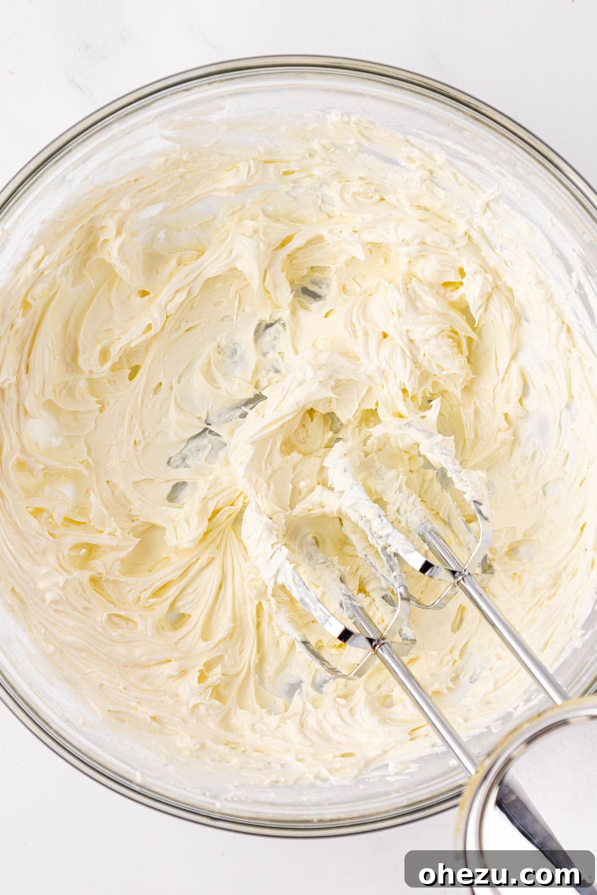 Softened cream cheese being whipped in a bowl until light and airy.