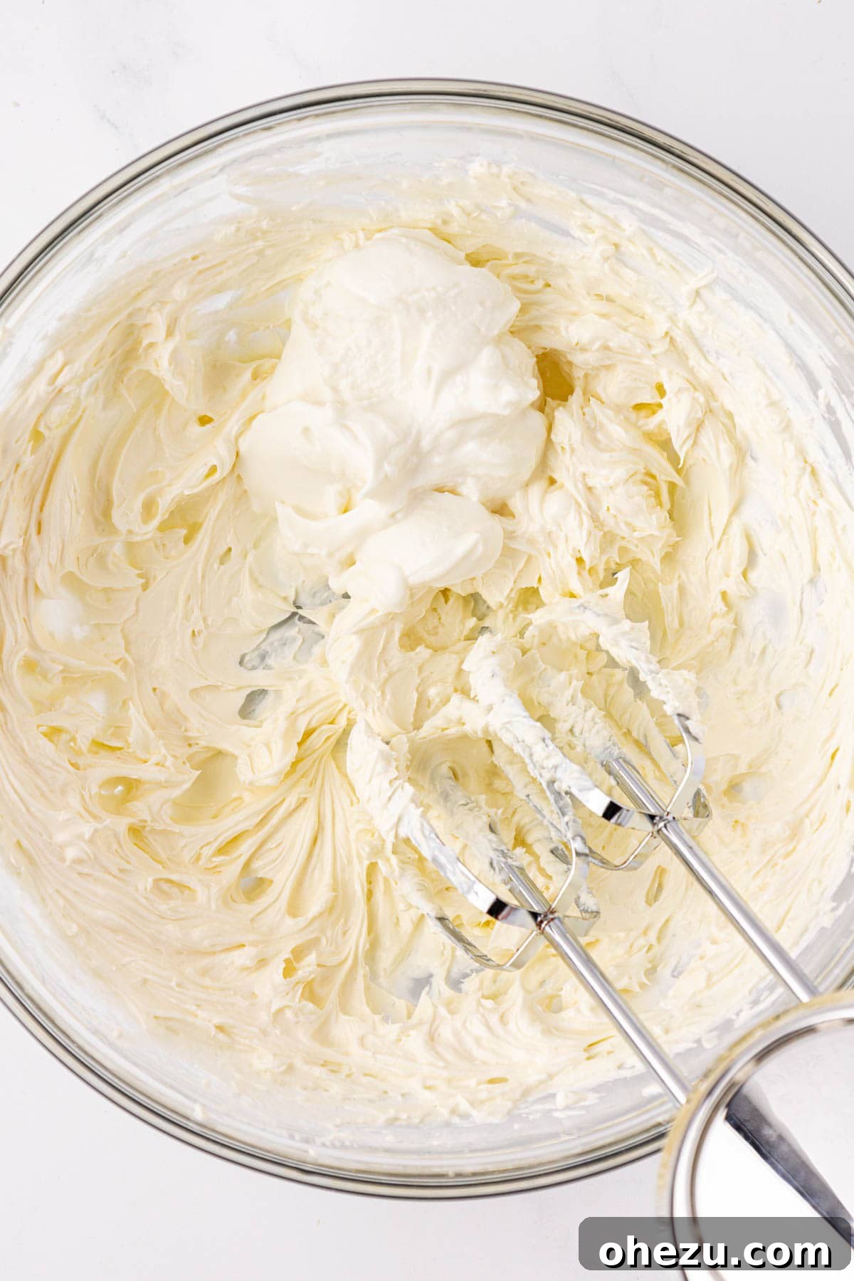 Adding plain Greek yogurt to the whipped cream cheese in a mixing bowl.