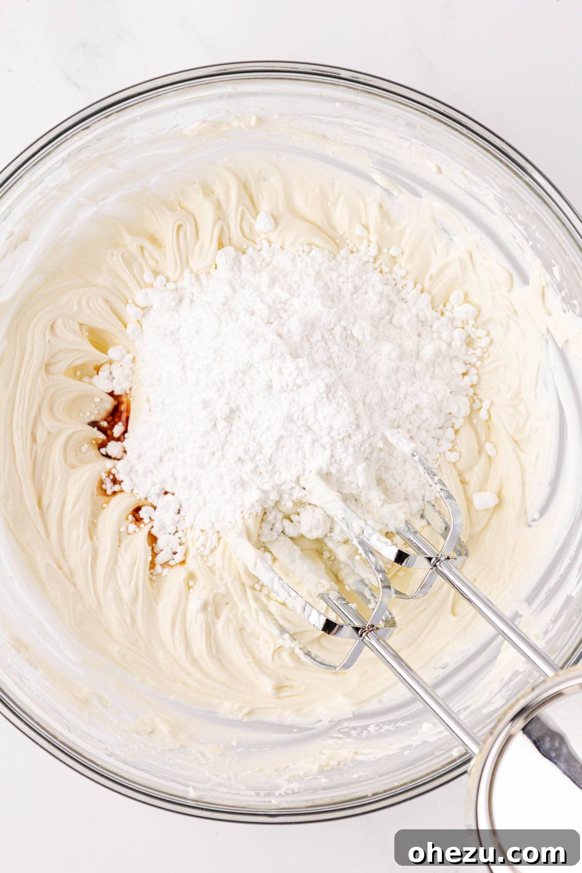 Powdered sugar and vanilla extract being added to the cream cheese and Greek yogurt mixture for frosting.