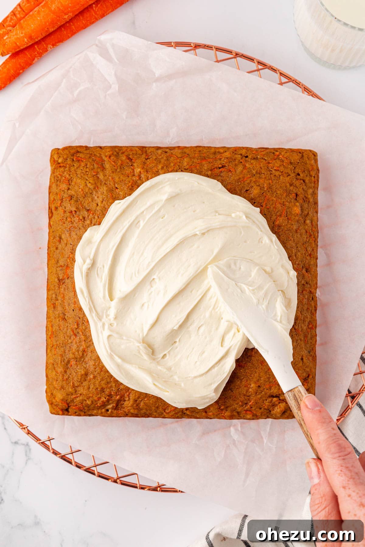 Spreading creamy white cream cheese frosting over the top of the cooled carrot cake.
