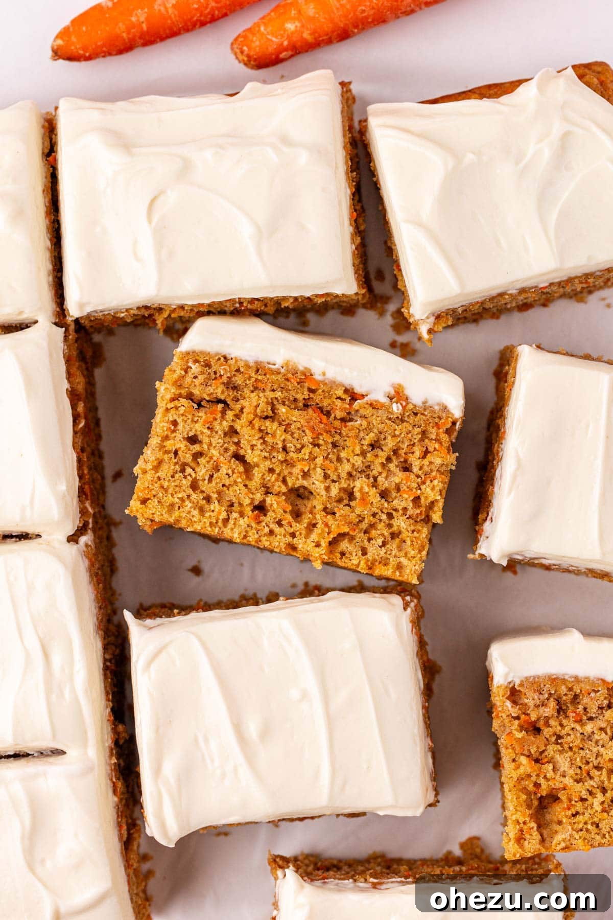 A plate stacked with multiple carrot cake snack bars, showing the moist cake and thick frosting.