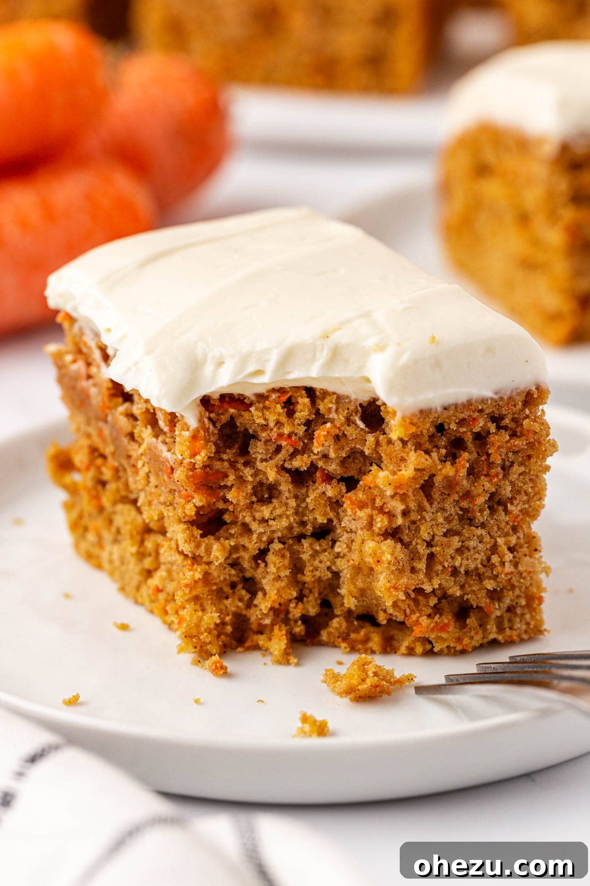 A close-up of a single carrot cake snack bar with a generous swirl of cream cheese frosting, showing its moist texture.