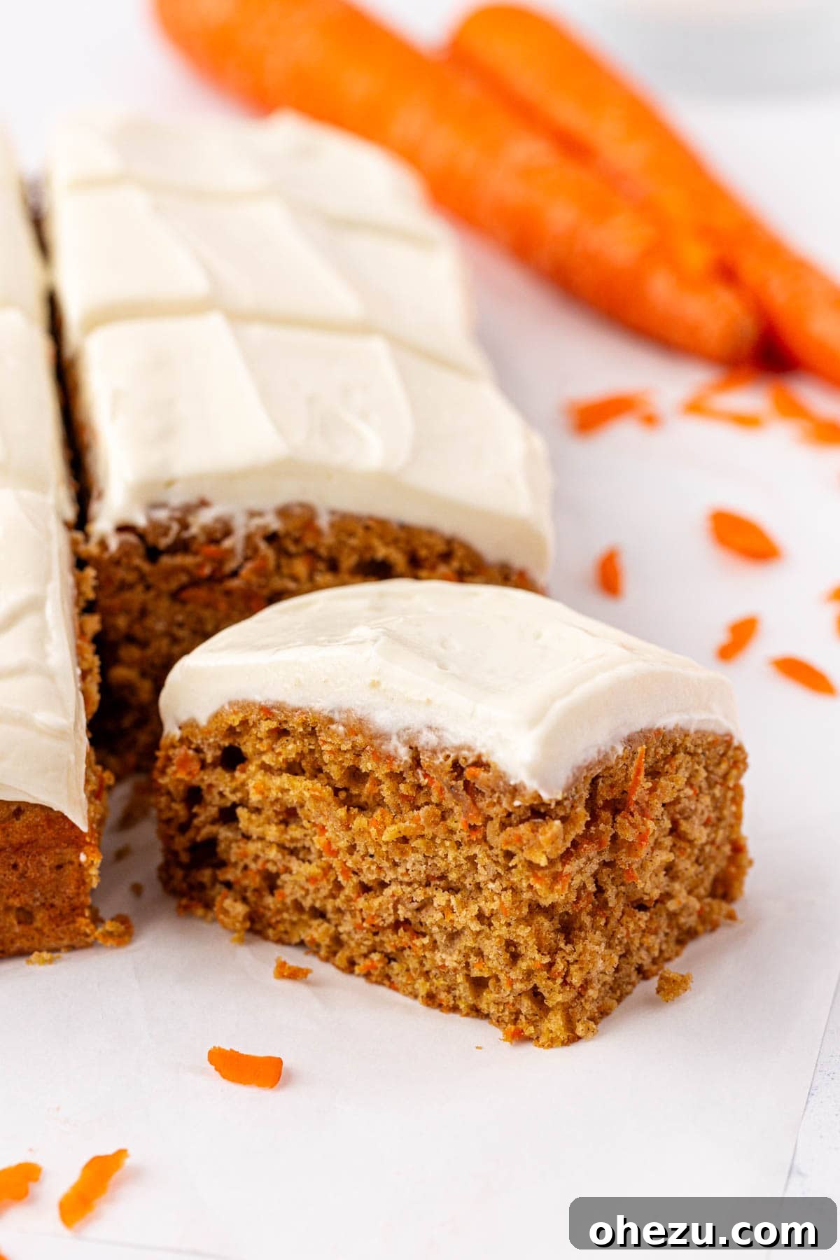 A single carrot cake snack bar being held, showing its perfectly cut edges and frosting.