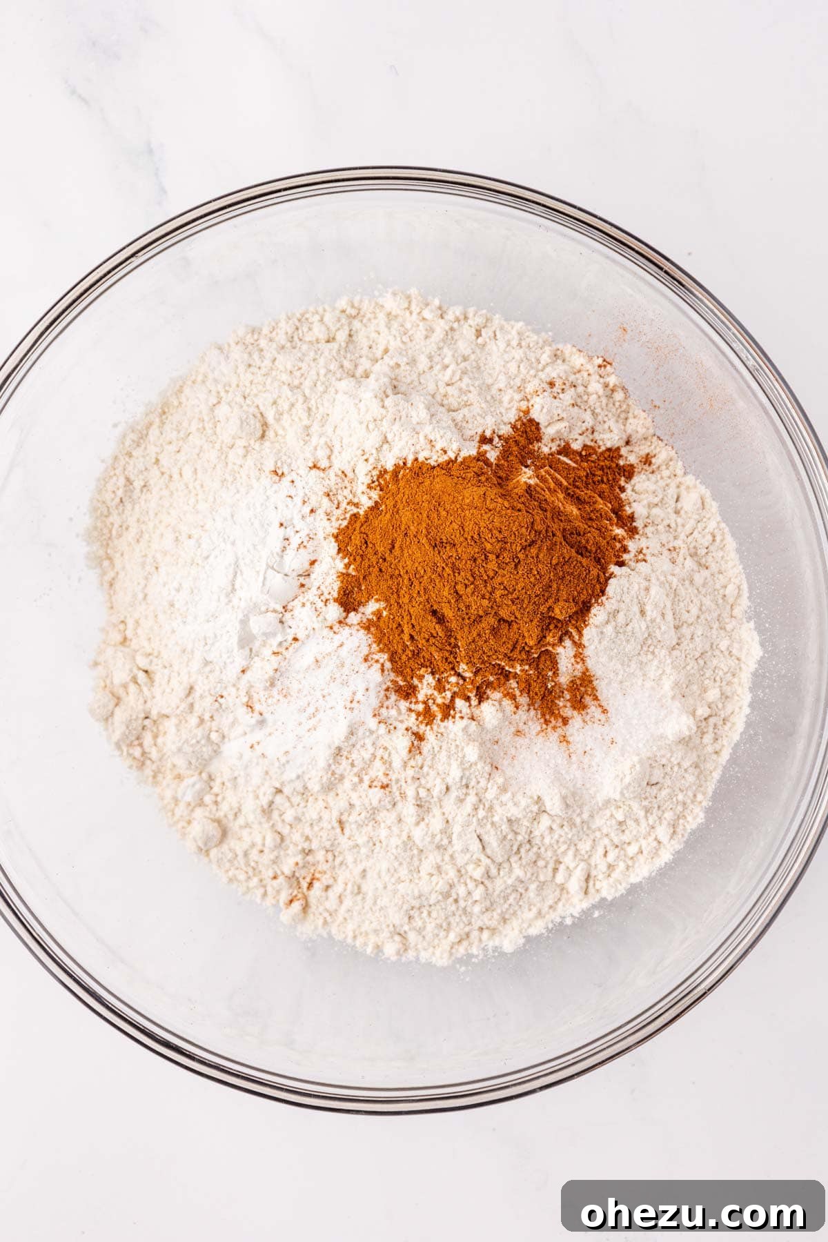 A bowl containing dry ingredients like flour, baking powder, baking soda, salt, and cinnamon before mixing.