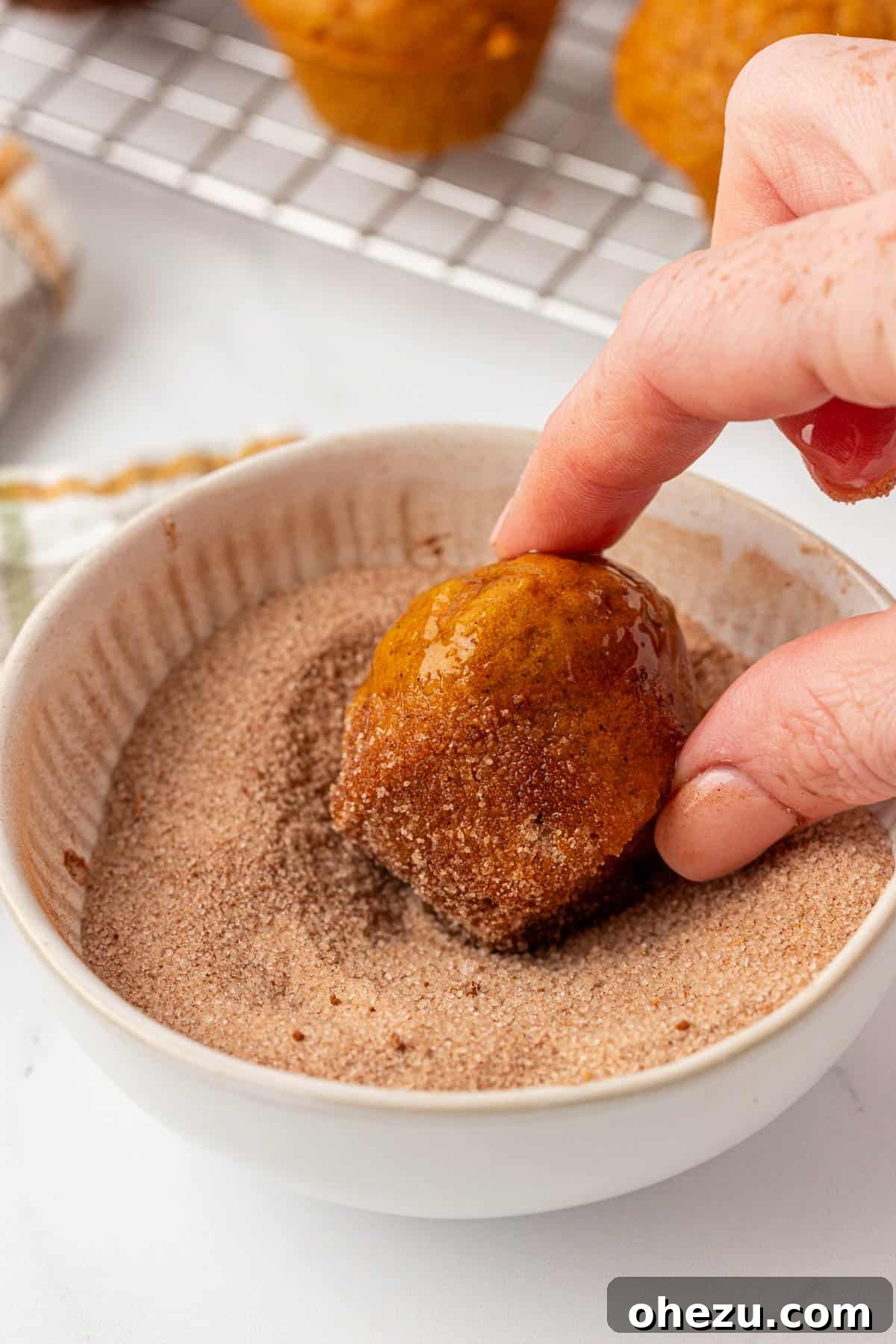 Spiced Pumpkin Donut Bites 13 A baked pumpkin mini muffin being carefully dipped into a bowl of melted butter