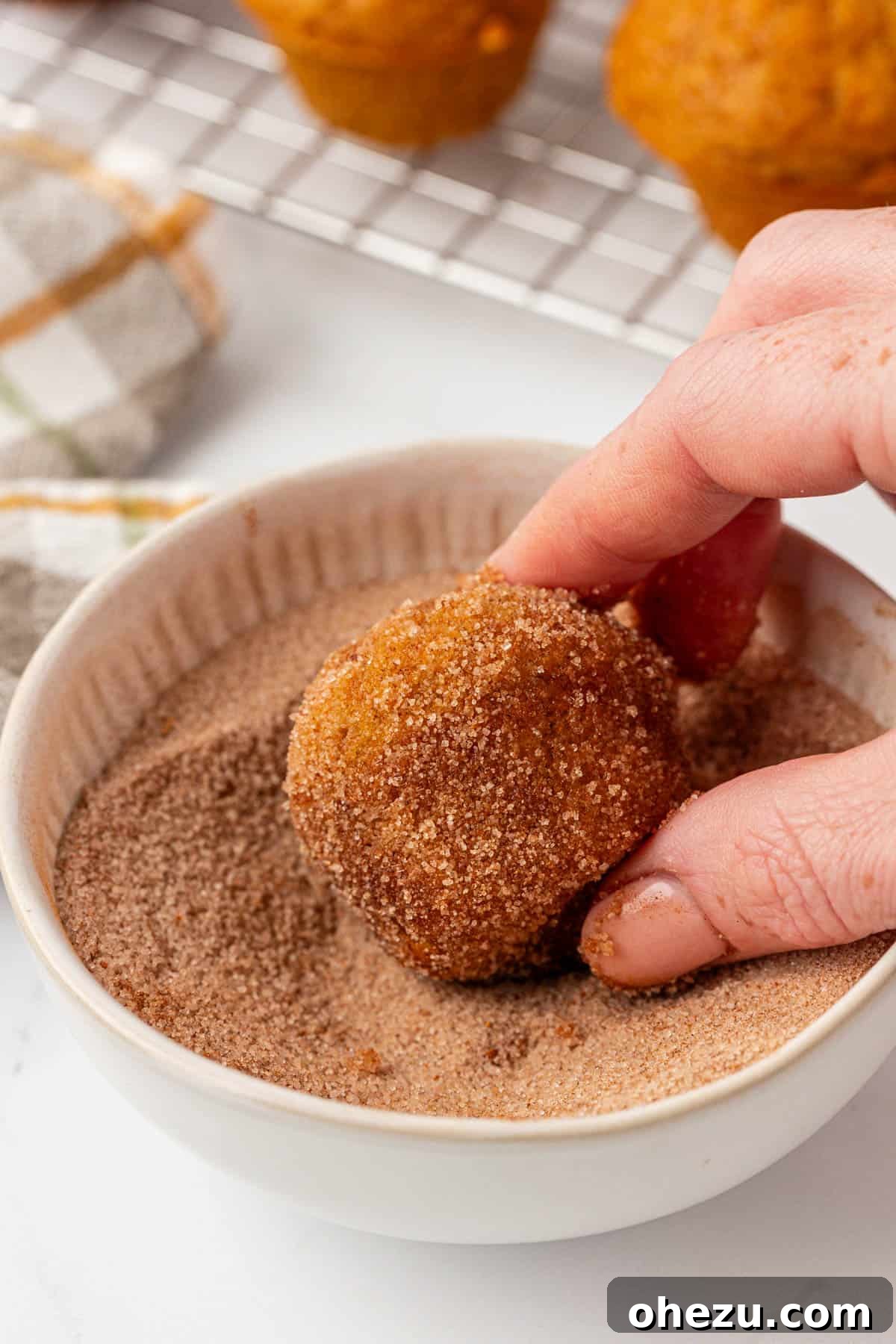 Spiced Pumpkin Donut Bites 14 A pumpkin mini muffin being rolled and coated in a bowl of cinnamon sugar