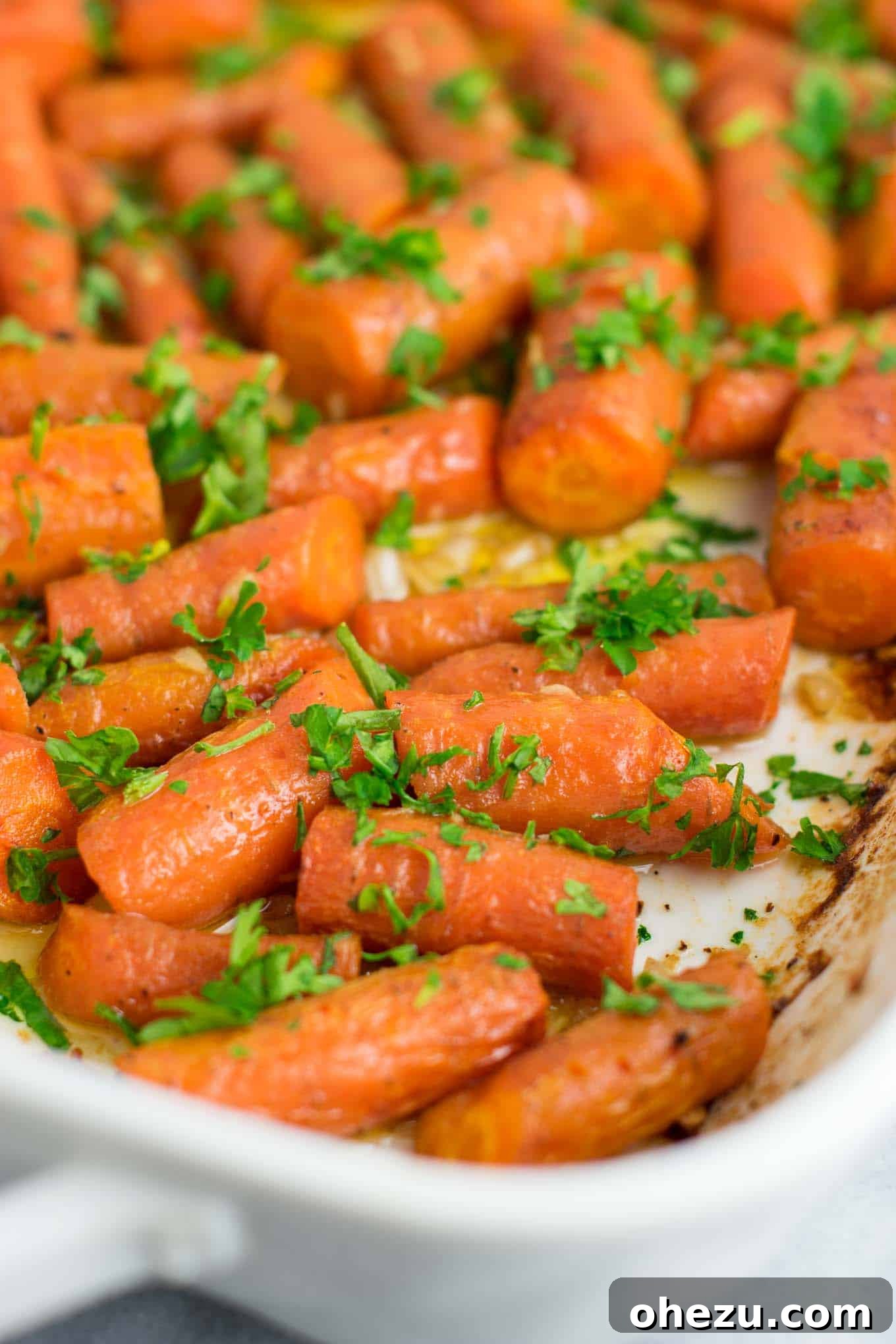 A serving dish filled with golden-brown garlic butter roasted carrots, generously topped with fresh parsley, ready to be enjoyed.