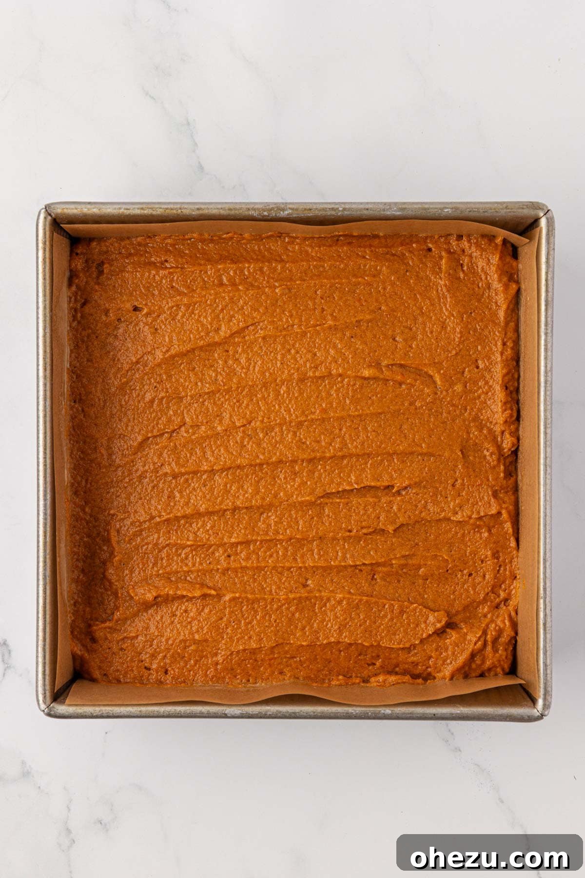 Pumpkin cake batter smoothly spread into an 8x8 inch baking pan