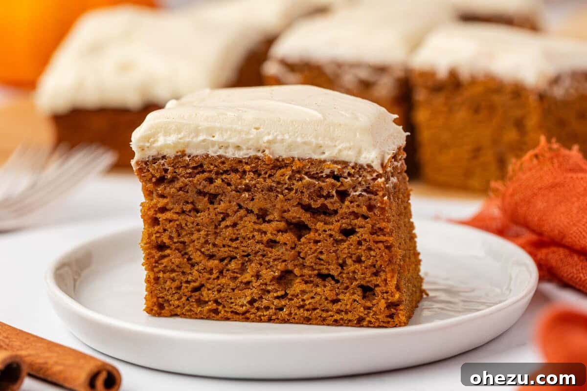 An appetizing slice of pumpkin cake with creamy frosting on a white plate, ready for consumption