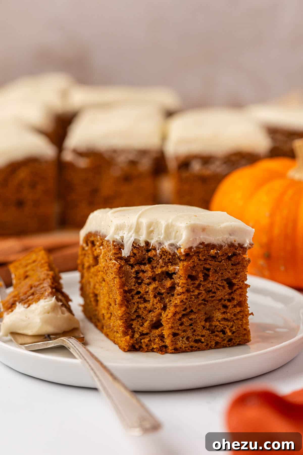 An inviting individual slice of pumpkin cake with rich cream cheese frosting on a pristine white plate