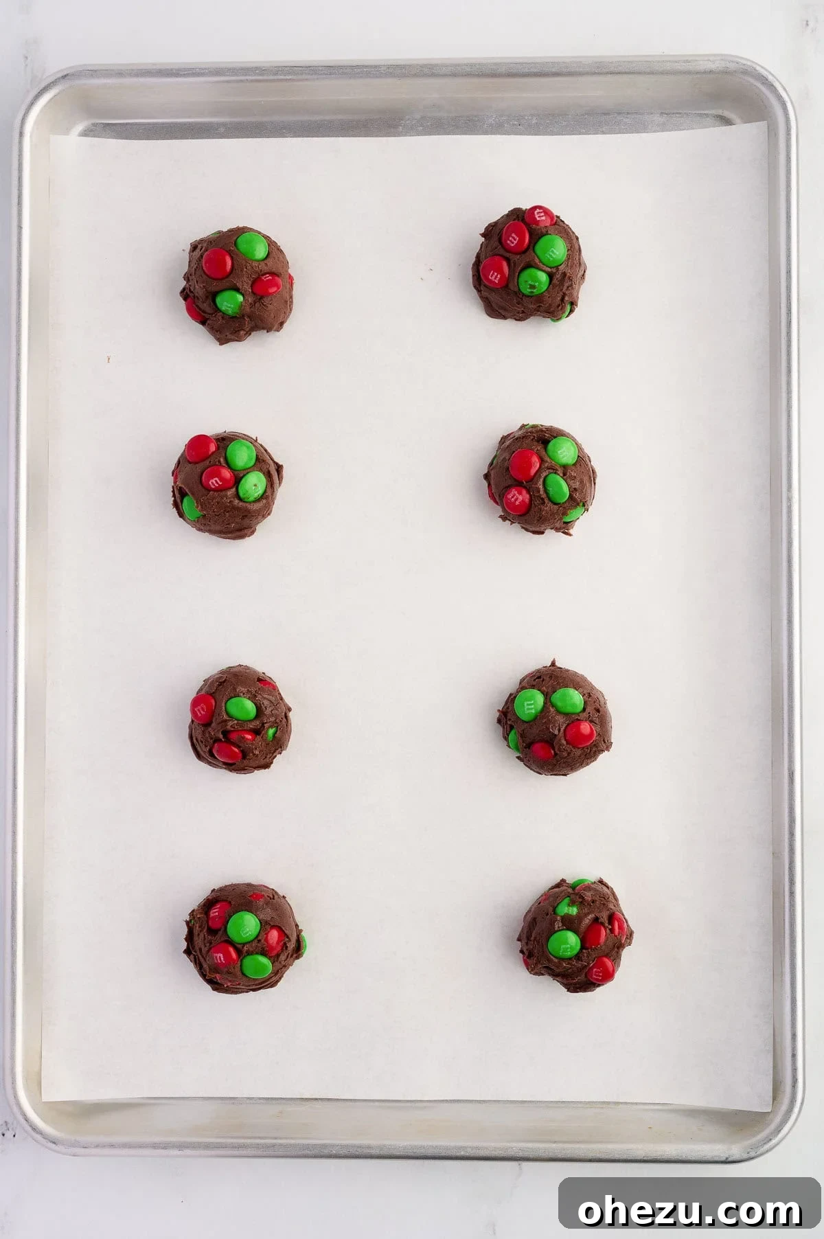balls of chocolate cookie batter with M&M's on a baking sheet