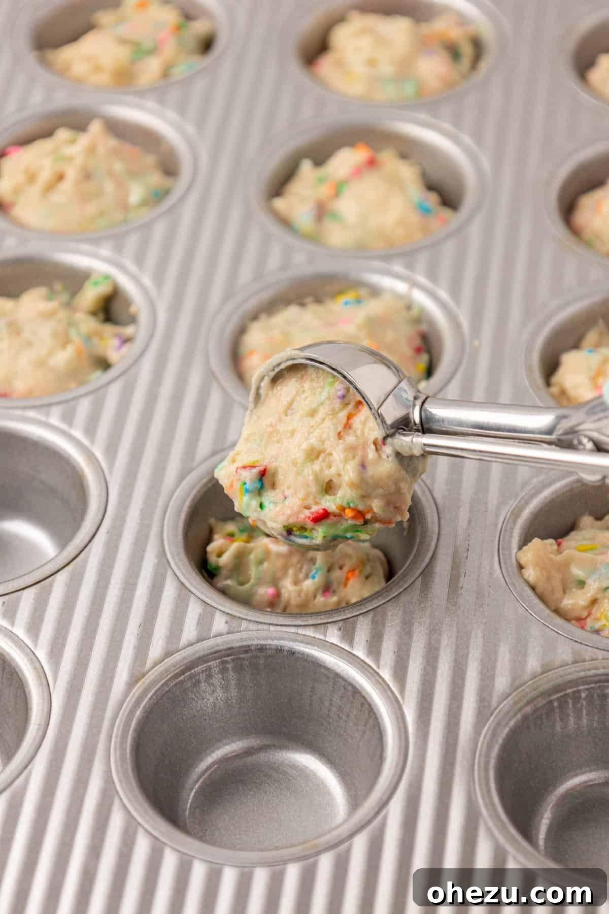 Scooping birthday cake muffin batter into a mini muffin tin