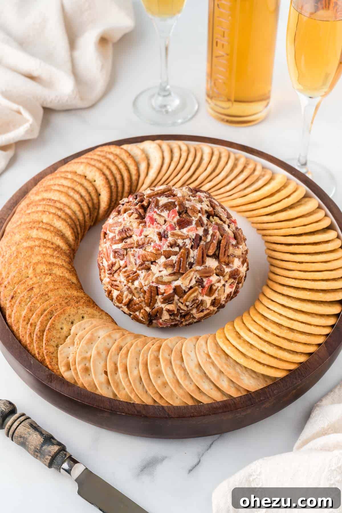 A festive pimento cheese ball, rolled in pecans and surrounded by an array of crackers on a decorative platter.