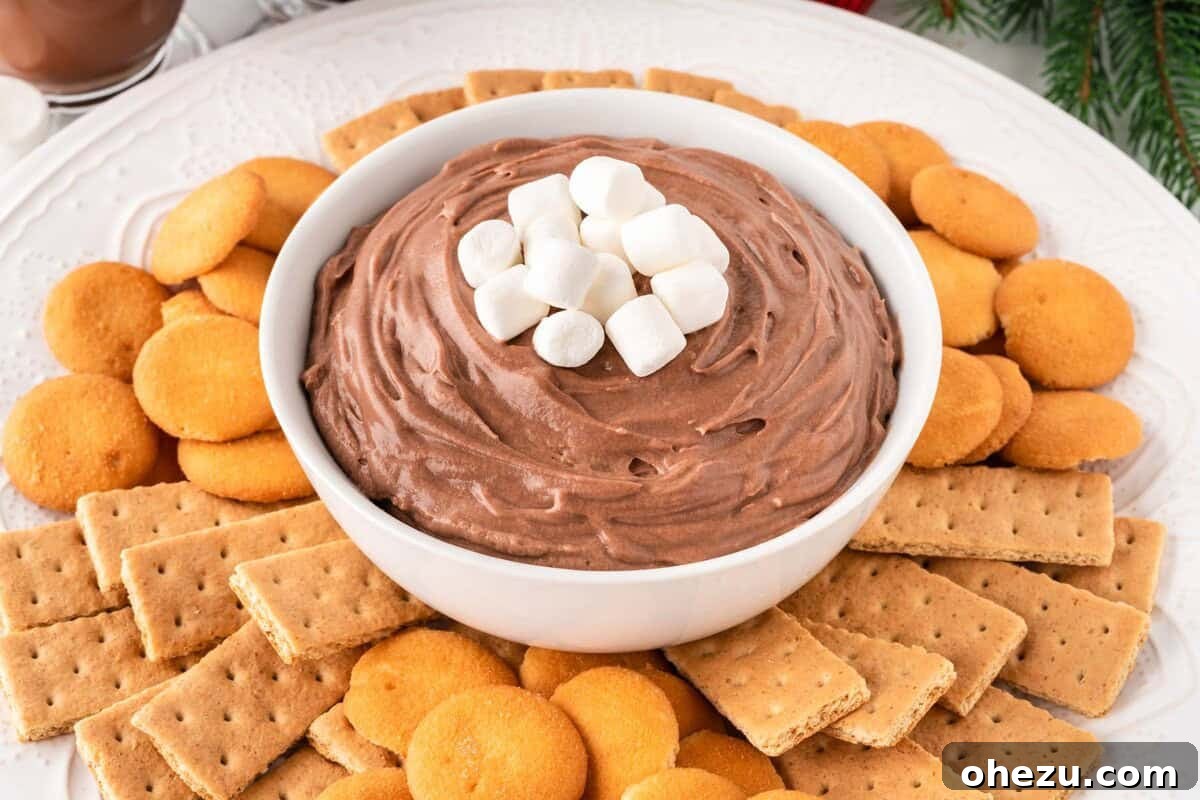 A charming bowl of hot chocolate dip, garnished with whipped cream and chocolate shavings, ready for a winter celebration.