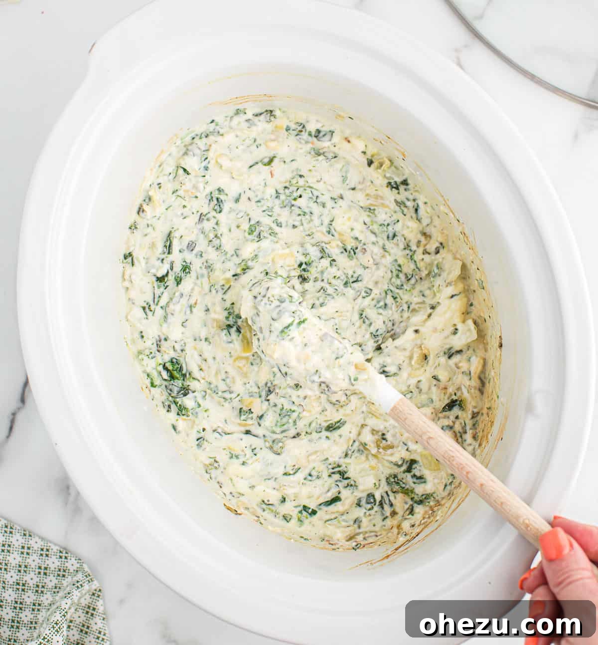 A close-up shot of creamy slow cooker spinach artichoke dip being stirred, highlighting its rich texture and melty cheese.