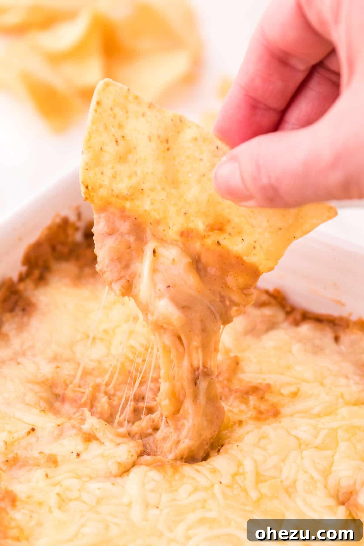 A crispy tortilla chip being dipped into a rich and creamy cream cheese bean dip, showcasing its smooth texture.