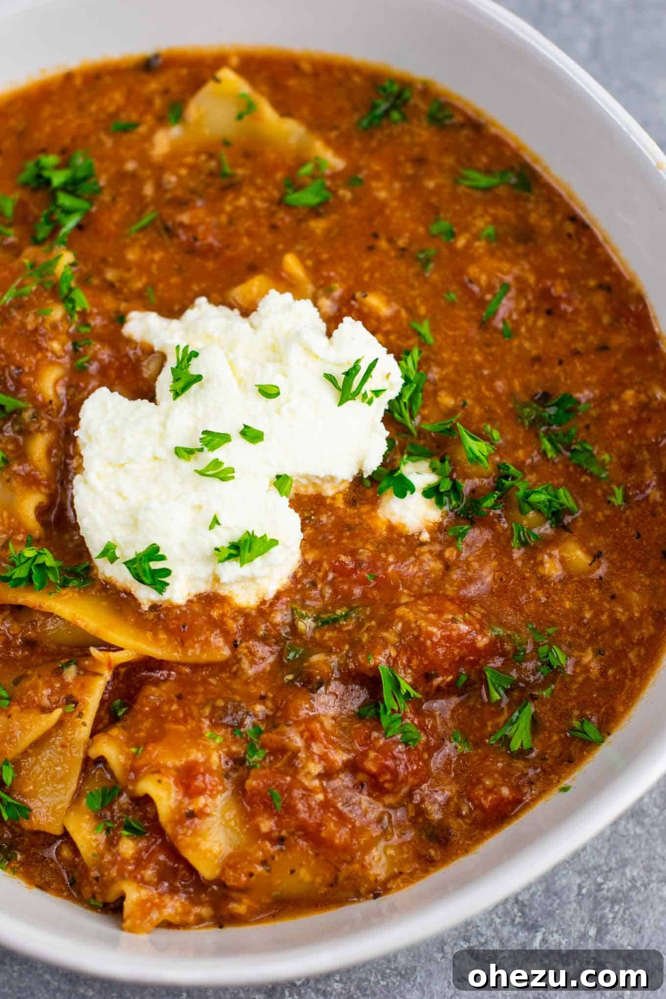 Bowl of hot vegetarian lasagna soup garnished with a generous dollop of ricotta cheese and fresh parsley, ready to be enjoyed.